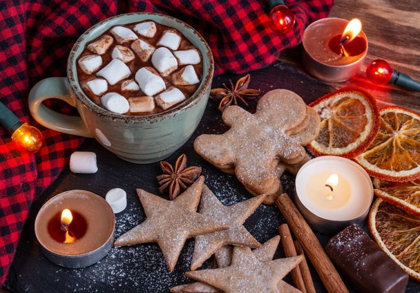 ατμοσφαιρική Χριστουγεννιάτικη σύνθεση, ένα φλιτζάνι κακάο με ζαχαρωτά, κεριά, μπισκότα μελόψωμου, γλυκά, κανέλα. - Φωτογραφία, εικόνα