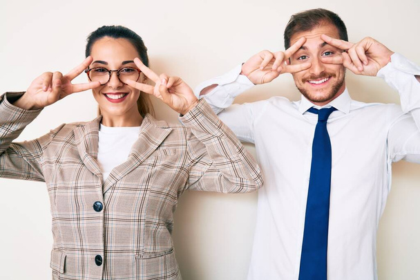 Beautiful couple wearing business clothes doing peace symbol with fingers over face, smiling cheerful showing victory  - Photo, Image