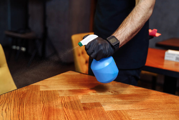 Close-up van de ober hand schoonmaken van de tafel met desinfecterende spray in een restaurant. Coronavirus bescherming tijdens de covid-19 pandemie in cafe. - Foto, afbeelding