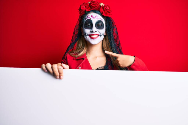 Frau im Totenkostüm hält leeres Transparent und zeigt mit dem Finger auf ein sich selbst lächelndes glückliches und stolzes  - Foto, Bild