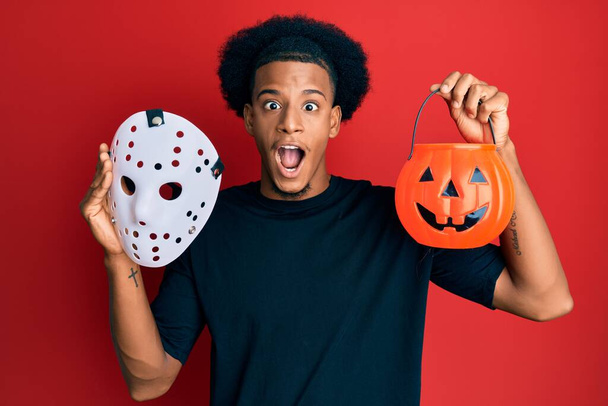 African american man with afro hair wearing hockey mask and halloween pumpking celebrating crazy and amazed for success with open eyes screaming excited.  - Valokuva, kuva