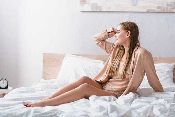 joyful young woman looking away while sitting on bed in modern bedroom  - Foto, imagen