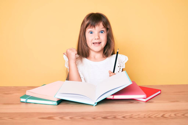 Uzun saçlı, okul sınavına çalışan beyaz bir kız çocuğu parmak ucunda ağzı açık bir şekilde gülümsüyor.  - Fotoğraf, Görsel