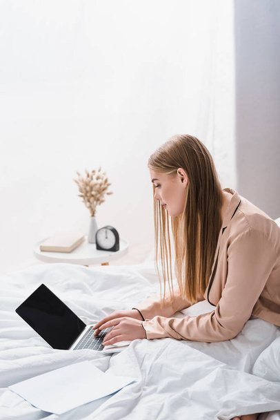 young freelancer in silk robe using laptop with blank screen in bedroom - Φωτογραφία, εικόνα