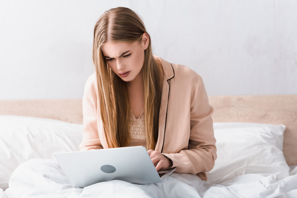 joven freelancer enfocado en bata de seda usando laptop en el dormitorio - Foto, imagen