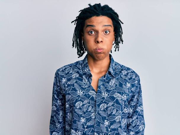 Junger afrikanisch-amerikanischer Mann in einem Hemd im 80er-Jahre-Stil, das Wangen mit lustigem Gesicht aufbläst. Mund mit Luft aufgeblasen, verrückter Ausdruck.  - Foto, Bild