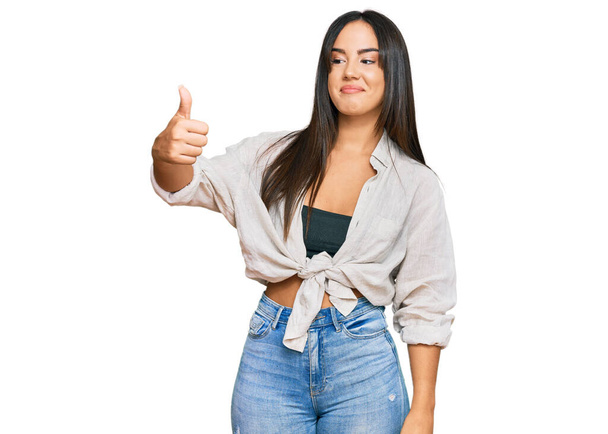 Young beautiful hispanic girl wearing casual clothes looking proud, smiling doing thumbs up gesture to the side  - Φωτογραφία, εικόνα