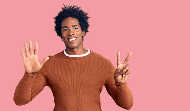 Bonito homem americano africano com cabelo afro vestindo roupas casuais mostrando e apontando para cima com os dedos número sete enquanto sorri confiante e feliz.  - Foto, Imagem