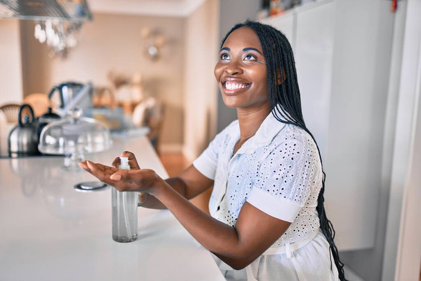 Jeune femme afro-américaine souriante heureuse à l'aide de gel désinfectant pour les mains à la maison - Photo, image