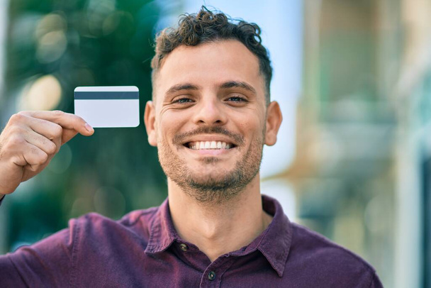 Jeune homme hispanique souriant heureux tenant carte de crédit à la ville. - Photo, image
