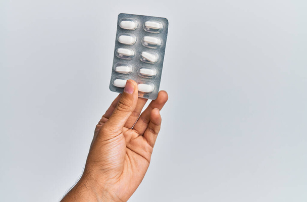 Рука латиноамериканца держит таблетки на изолированном белом фоне. - Фото, изображение