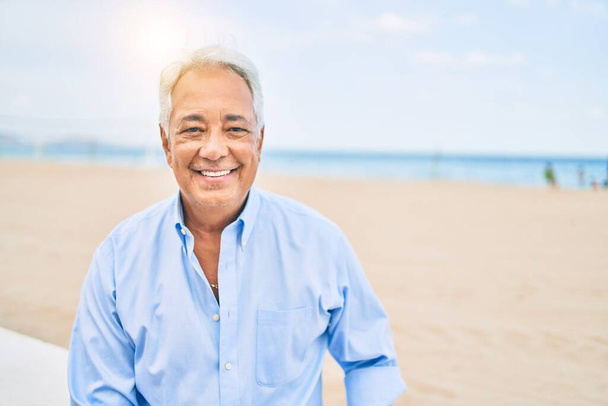 Handosme його латиноамериканський чоловік з сірим волоссям посміхається щасливим на пляжі, насолоджуючись відпусткою влітку
 - Фото, зображення