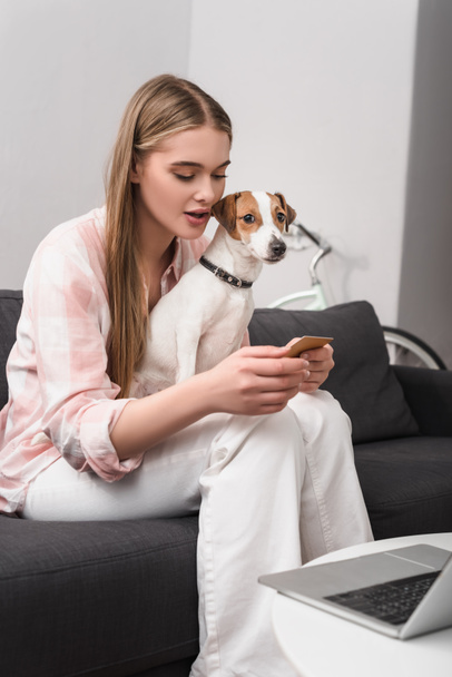 young woman holding credit card near dog and laptop on coffee table - Foto, Bild