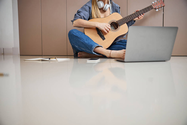 Female musician playing guitar and using laptop at home - Φωτογραφία, εικόνα