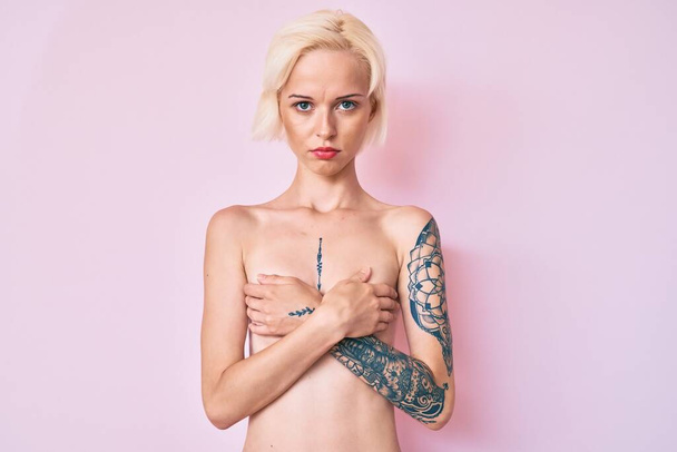 Fiatal szőke nő tetoválás áll félmeztelen depressziós és aggódni a szorongás, sír dühös és fél. szomorú kifejezés.  - Fotó, kép