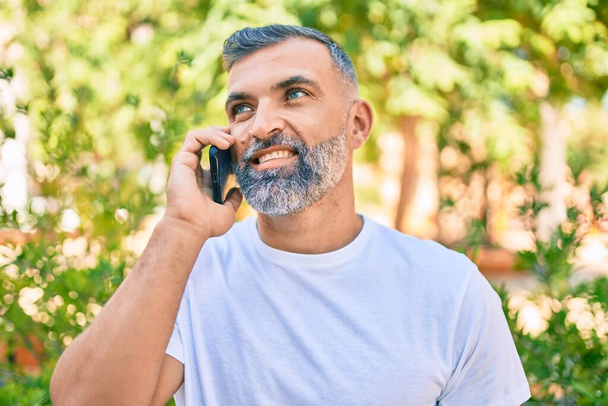 Середньовічний чоловік сіро-волохатий посміхається щасливо розмовляти по смартфону в парку
 - Фото, зображення