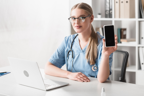 veterinarian in glasses holding smartphone with blank screen near laptop on desk - 写真・画像