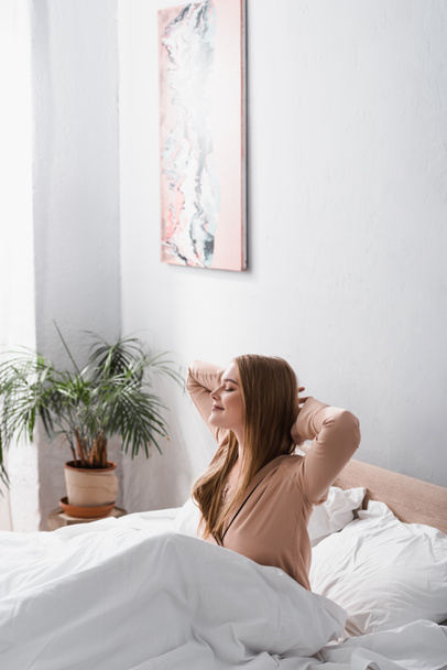 awake and cheerful woman in silk pajamas stretching in bed - Zdjęcie, obraz
