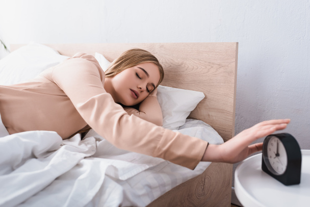 sleepy woman reaching alarm clock on bedside table  - Photo, Image