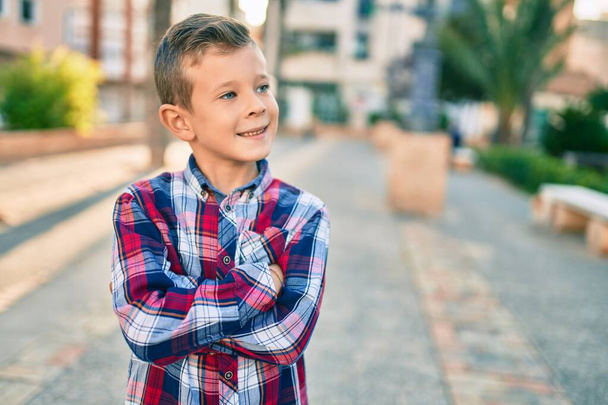 Adorabile ragazzo caucasico con le braccia incrociate sorridente felice in piedi alla città. - Foto, immagini