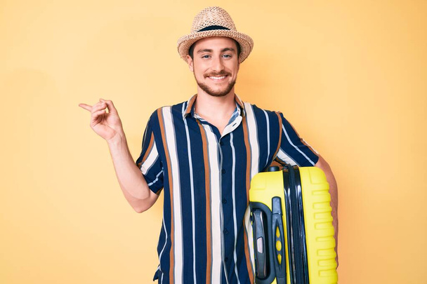 Молодой красивый мужчина в летней шляпе, держа сумку, улыбаясь счастливо указывая рукой и пальцем в сторону.  - Фото, изображение