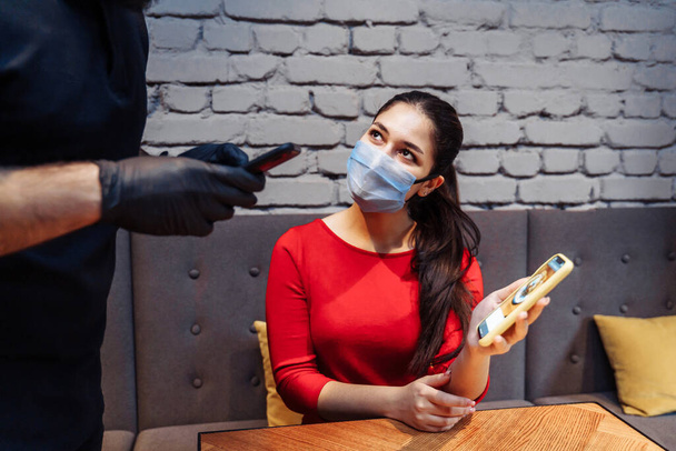 Soziale Distanzierung während der Covid-19-Coronavirus-Pandemie. Ein Restaurantbesucher mit Gesichtsmaske bestellt telefonisch über die Speisekarte. Online-Menüs verhindern die Ausbreitung von Infektionen. - Foto, Bild