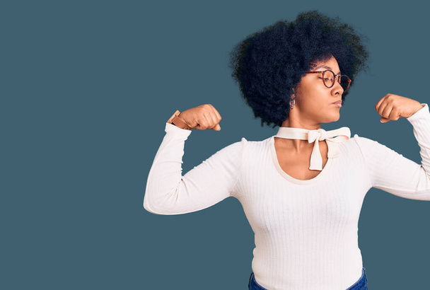 Молодая африканская американская девушка в повседневной одежде и очках, показывающая мышцы рук, улыбающиеся с гордостью. фитнес концепция.  - Фото, изображение