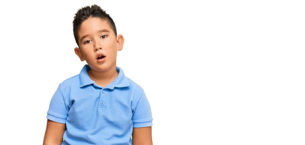 Μικρό αγόρι ισπανόφωνο παιδί που φοράει καθημερινά ρούχα στο πρόσωπο σοκ, δείχνοντας δύσπιστος και σαρκαστικός, έκπληκτος με ανοιχτό στόμα  - Φωτογραφία, εικόνα