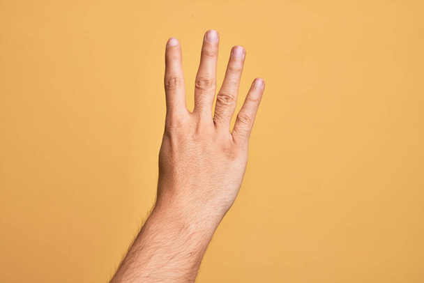Hand of caucasian young man showing fingers over isolated yellow background counting number 4 showing four fingers - Фото, изображение