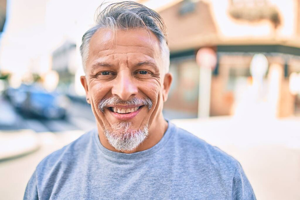 Латиноамериканец средних лет седой мужчина улыбается счастливо стоя в городе. - Фото, изображение