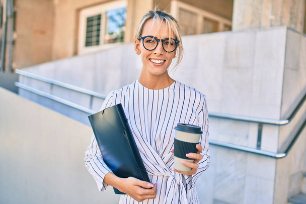 Jovem mulher de negócios loira sorrindo bebida feliz tirar café na cidade. - Foto, Imagem