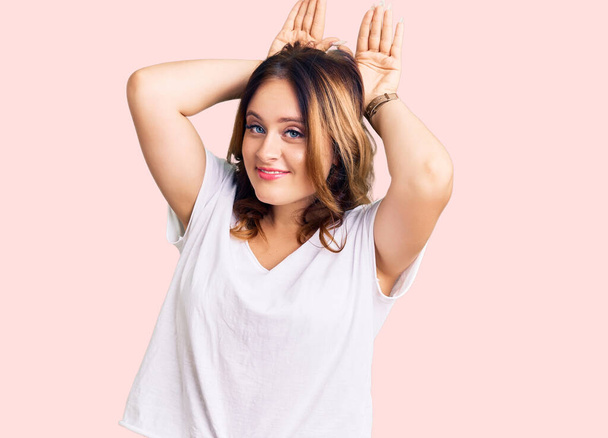 Young beautiful caucasian woman wearing casual white tshirt doing bunny ears gesture with hands palms looking cynical and skeptical. easter rabbit concept.  - Photo, Image
