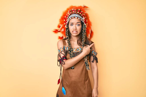 Молодая красивая латинская девушка в индийском костюме указывая в сторону взволнованный и нервный указательным пальцем, обеспокоенное и удивленное выражение лица  - Фото, изображение