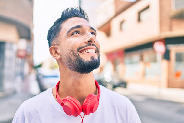 若いアラブ人の男は、街を歩くヘッドフォンを使用して幸せな笑顔. - 写真・画像
