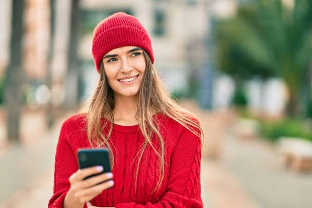 Fiatal spanyol nő visel téli stílus okostelefon a városban. - Fotó, kép