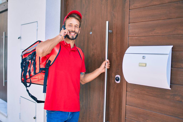 sian delivery man wearing red uniform and delivery backpack smilly happy outdoors speaking on the phone - 写真・画像