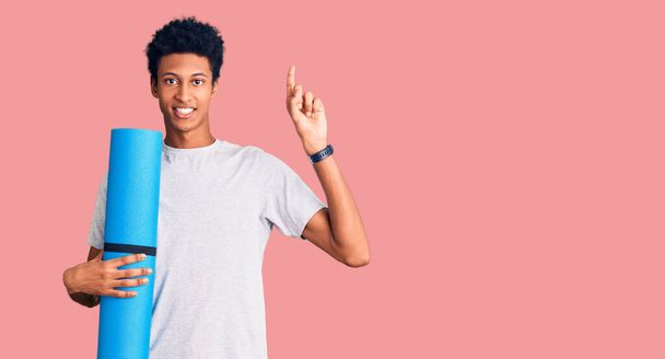 若いですアフリカ系アメリカ人男性保持ヨガマット驚くですアイデアや質問指差し指とともに幸せな顔,ナンバーワン  - 写真・画像