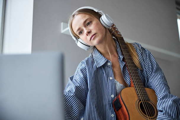 Charming young woman with guitar using laptop at home - Foto, immagini