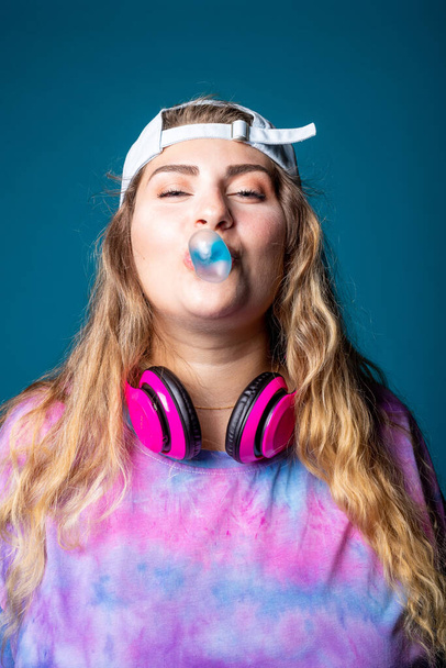 Caucasian woman blowing bubble gum playful chewing gum isolated on blue background wearing vintage 80's clothes - Foto, imagen