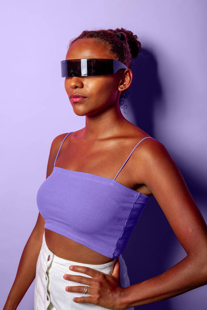 Молодая черная женщина в фантастических умных очках, изолированных на фиолетовом фоне наслаждаясь дополненной реальностью - Фото, изображение