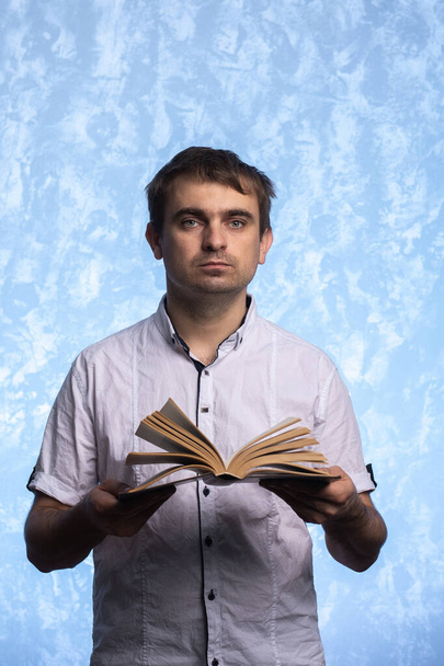 een jongeman met een Europees uiterlijk in een wit hemd houdt een open boek in zijn handen. close-up portret. studenten die zich voorbereiden op examens. onderwijsconcept - Foto, afbeelding