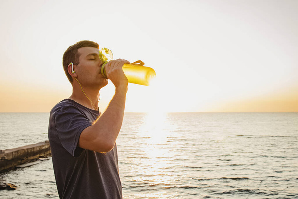 Man drinking water from the bottle after the jogging near the sea - Φωτογραφία, εικόνα