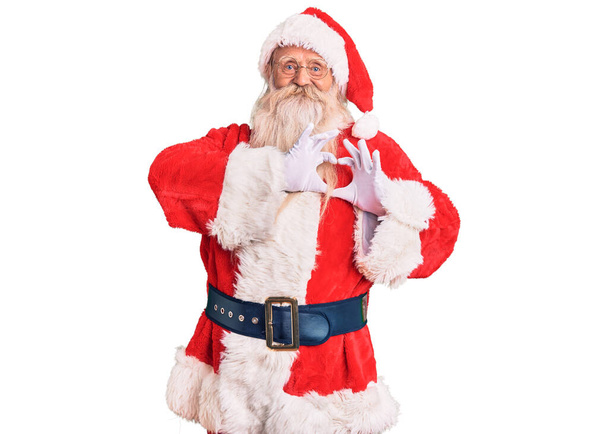 Старик с седыми волосами и длинной бородой в традиционном костюме Санта Клауса, улыбающийся в любви и делающий символическую форму сердца руками. романтическая концепция.  - Фото, изображение
