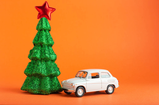 Christmas New Year tree with red star on top near white car toy. Creative miniature Xmas tree and car on Orange color background.. Gift delivery concept - Фото, изображение