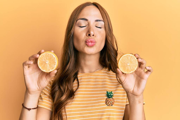 Jeune femme brune tenant orange frais regardant la caméra souffler un baiser étant belle et sexy. expression d'amour.  - Photo, image