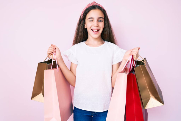 Menina hispânica bonito segurando sacos de compras piscando olhando para a câmera com expressão sexy, rosto alegre e feliz.  - Foto, Imagem