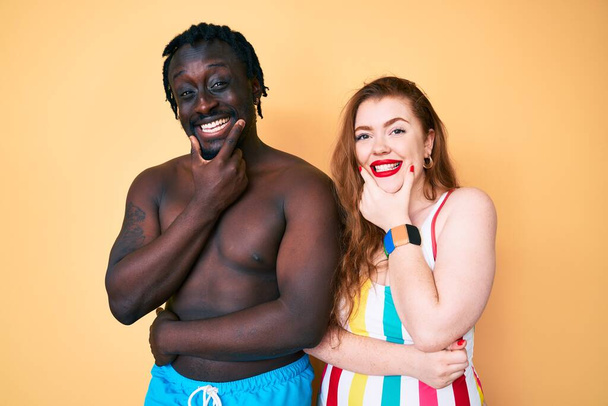 Couple Interracial en maillot de bain regardant avec confiance la caméra souriant avec les bras croisés et la main levée sur le menton. penser positivement.  - Photo, image
