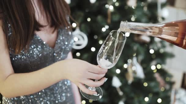 Egy nő rózsás pezsgőt önt egy pohárba egy karácsonyfával a háttérben. - Felvétel, videó