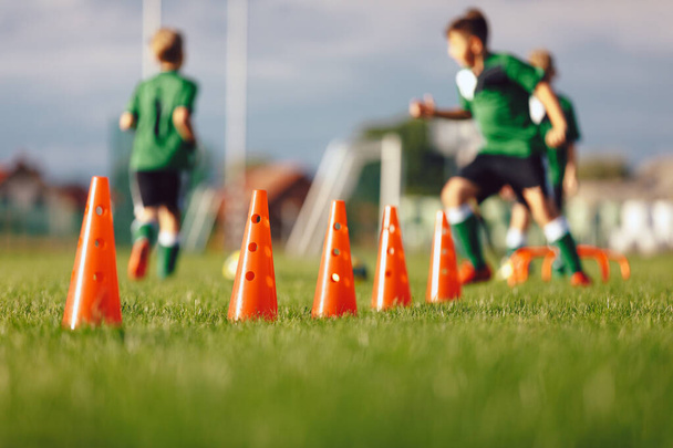 Fußballslalomdrill-Trainingsgeräte. Reihe von roten Trainingskegeln. Jungen laufen Bälle im Hintergrund. Soccer Grass Training Rasenplatz - Foto, Bild