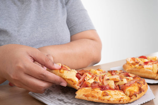 Голодная женщина с избыточным весом держит пиццу и с радостью ест пиццу. Концепция расстройства пищевого опьянения (BED) и расслабления с употреблением вредной пищи и нездоровой пищи. - Фото, изображение